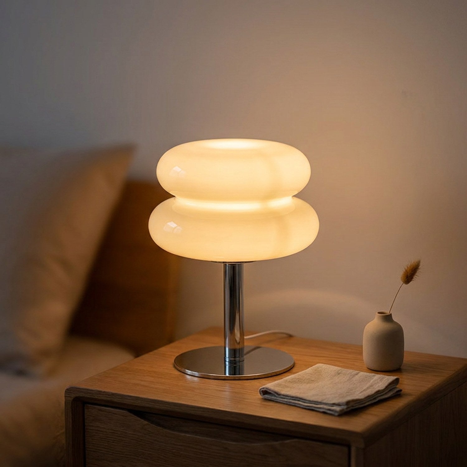 Lampe de chevet en verre forme macaron beige allumée sur une table de nuit