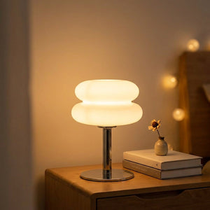 Lampe de chevet en verre forme macaron blanche allumée sur une table de nuit