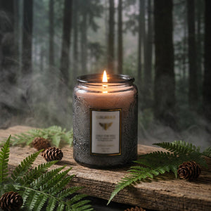 Bougie parfumée Forêt Brumeuse en pot de verre gris sur bois avec fougère et brume forestière