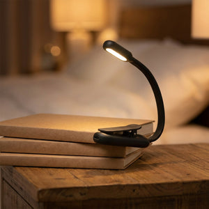 Lampe de lecture à clipser noire allumée posée sur une pile de livres
