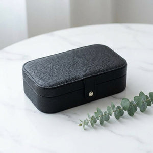 Boîte à bijoux voyage noire en simili cuir sur surface en marbre