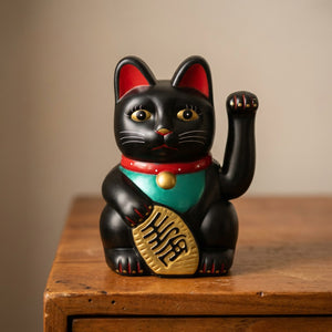 Figurine chat porte-bonheur noir posé sur une surface en bois avec fond chaleureux