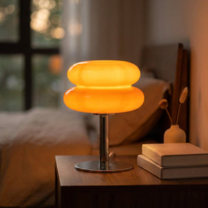 Lampe de chevet en verre forme macaron orange allumée sur une table de nuit
