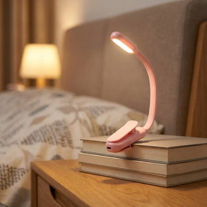 Lampe de lecture à clipser rose allumée posée sur une pile de livres