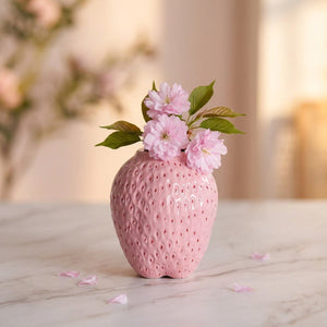 Petit vase rose en forme de fraise ronde garni de fleurs de cerisier