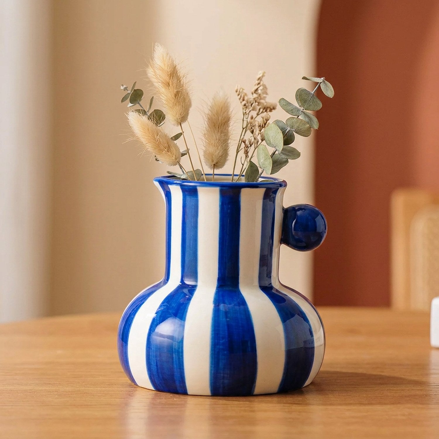 Vase en céramique à rayures bleues garni de fleurs séchées sur une table en bois