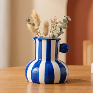 Vase en céramique à rayures bleues garni de fleurs séchées sur une table en bois