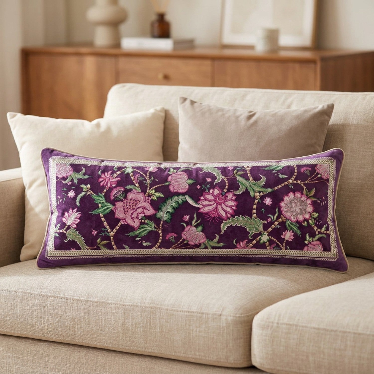 Housse de coussin rectangulaire en velours violet au motif floral rose posée sur un canapé beige