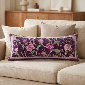 Housse de coussin rectangulaire en velours violet au motif floral rose posée sur un canapé beige