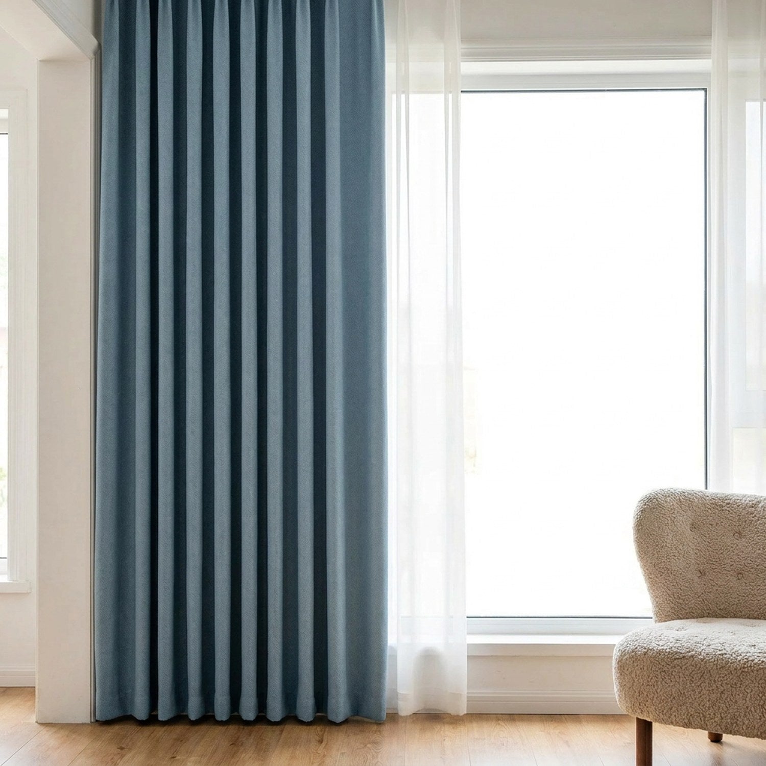 Rideau occultant bleu suspendu devant une fenêtre lumineuse avec fauteuil beige