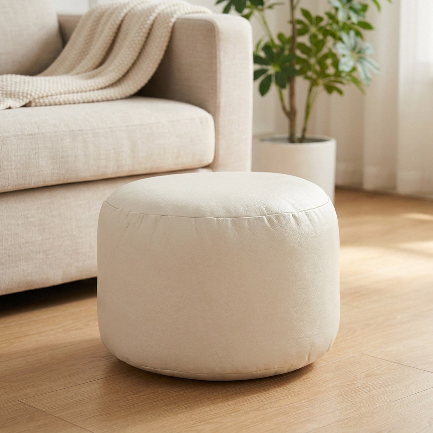 Pouf marocain rond en simili cuir crème posé sur un parquet clair