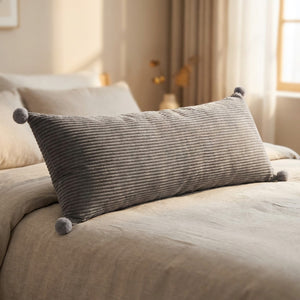 Coussin long en velours côtelé gris orné de pompons sur un lit