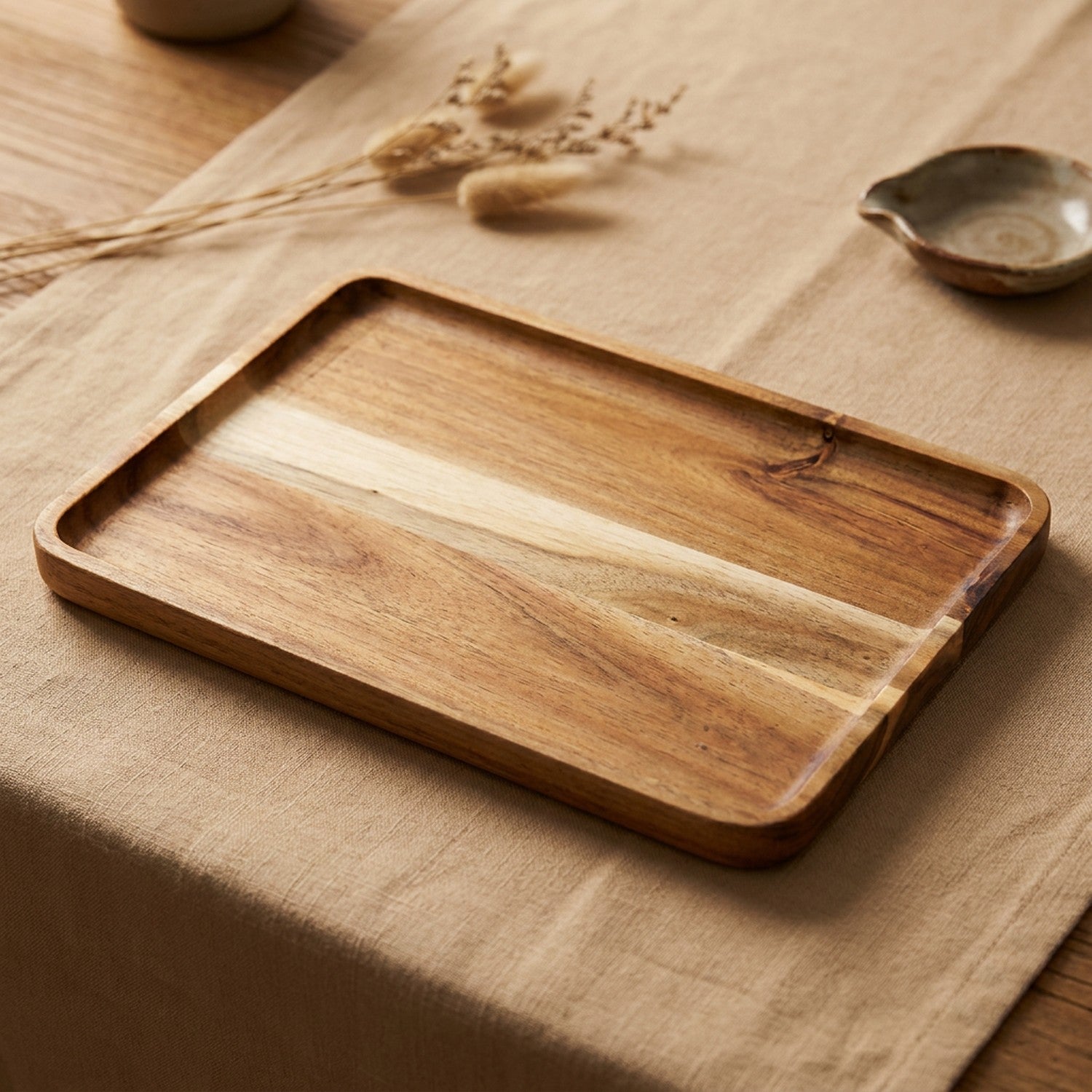 Plateau rectangulaire en bois d'acacia posé sur une nappe en lin beige