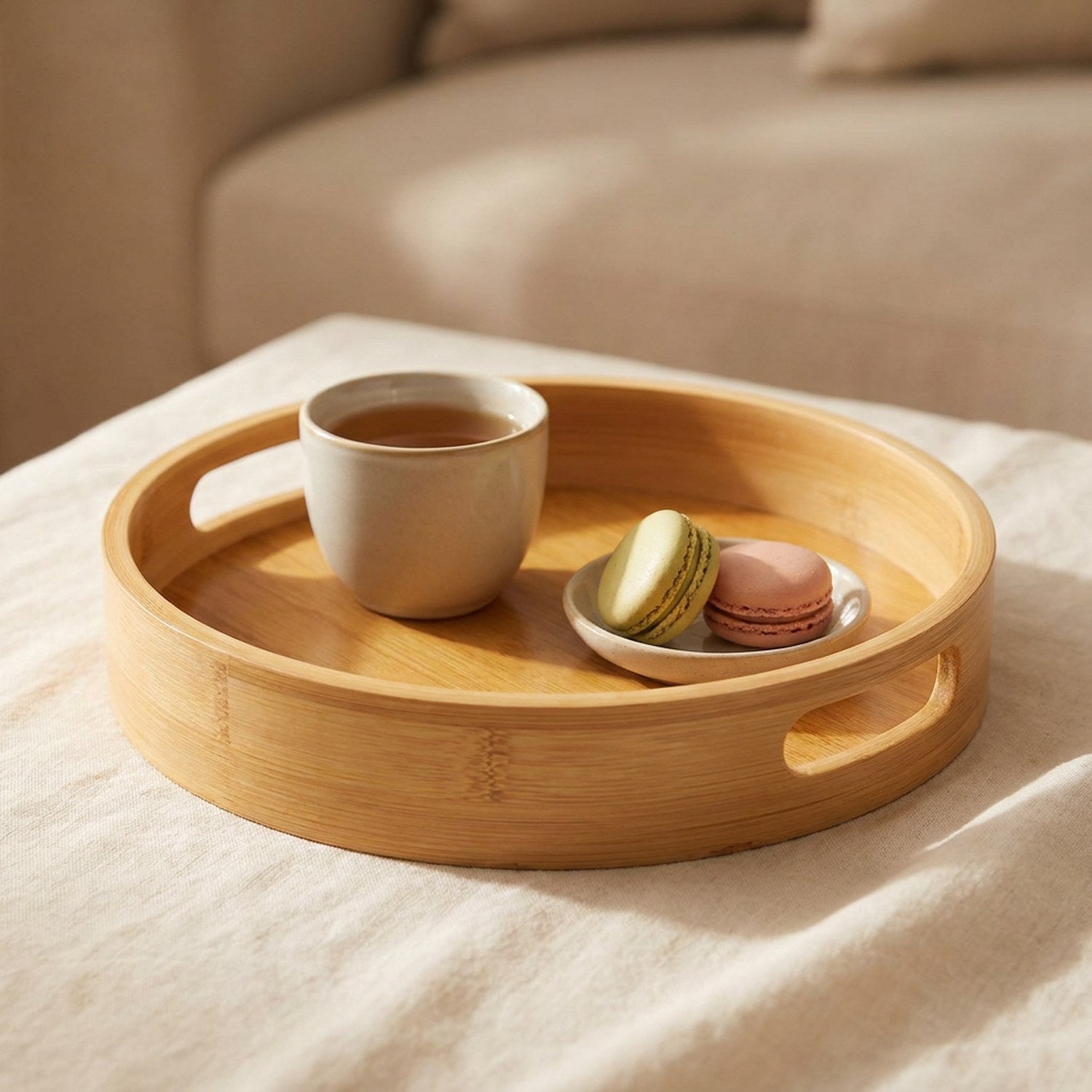 Plateau de service rond en bambou avec thé et macarons sur du linge clair