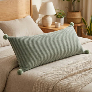 Coussin long en velours côtelé vert sauge orné de pompons sur un lit