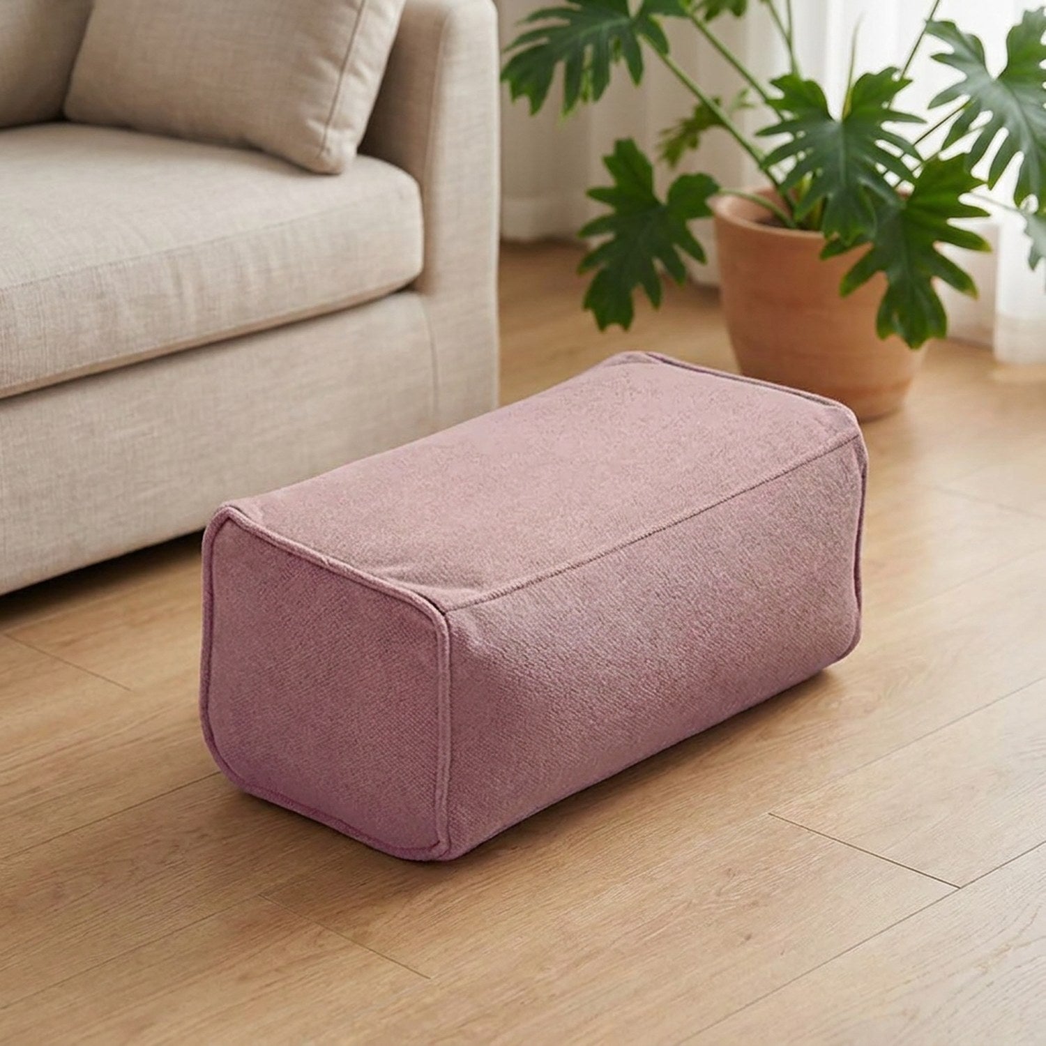 Pouf repose-pieds en chenille vieux rose posé sur un parquet clair