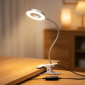 Lampe pince argentée à col de cygne allumée clipsée sur un bureau