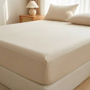 Drap housse beige délavé installé sur un matelas dans une chambre chaleureuse