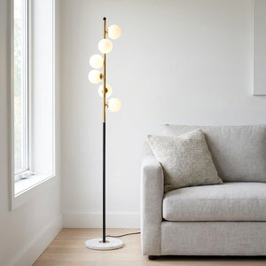 Lampadaire à 5 boules de verre blanc laiteux sur tige noire et dorée dans un salon moderne