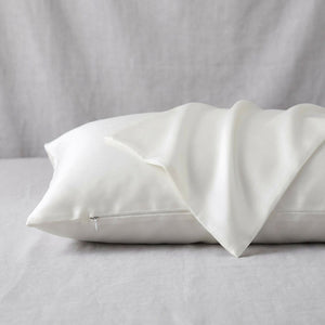 Taie d'oreiller en soie blanche ivoire posée sur un tissu de lin gris clair