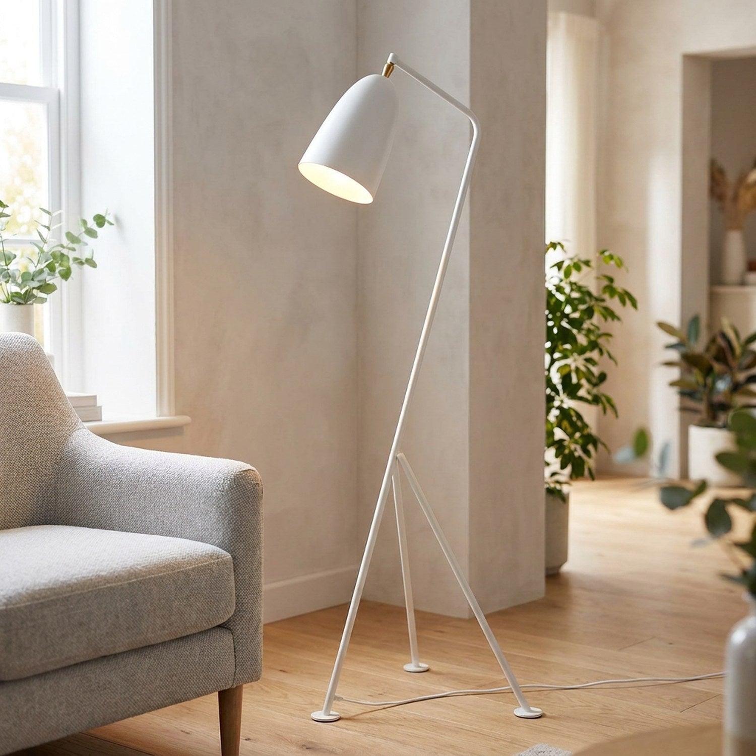 Lampadaire trépied blanc dans un salon lumineux avec fauteuil gris clair