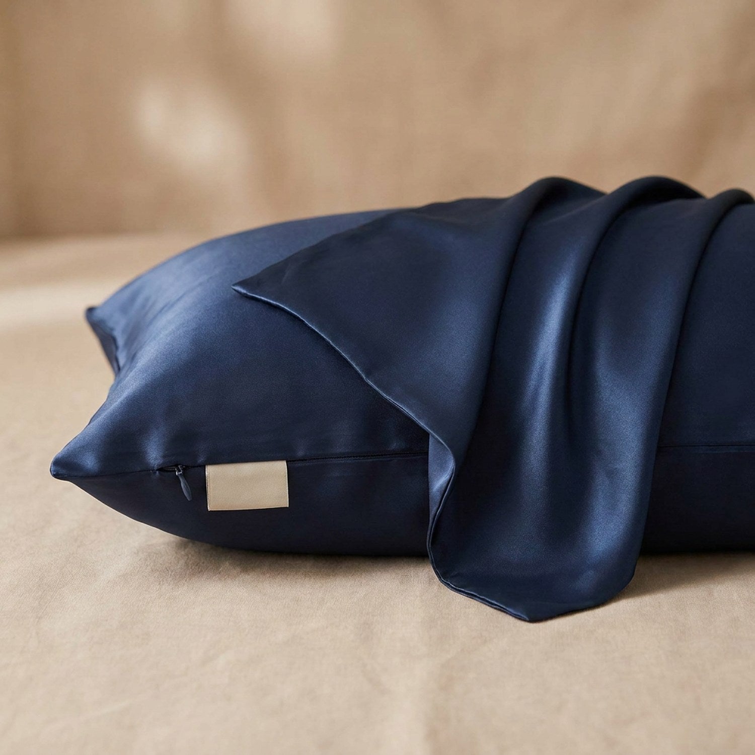 Taie d'oreiller en soie bleu foncé posée sur un tissu de lin beige