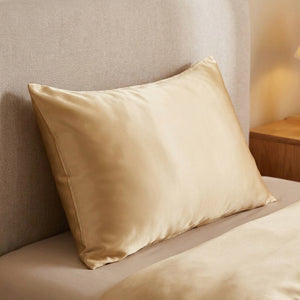 Taie d'oreiller satin dorée posée sur un lit contre une tête de lit