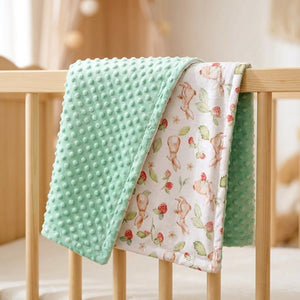 Couverture bébé minky réversible vert menthe à motif lapins pliée sur un lit à barreaux