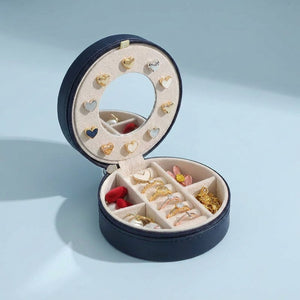 Coffret à bijoux de voyage bleu marine ouvert sur fond bleu clair avec bijoux en coeur