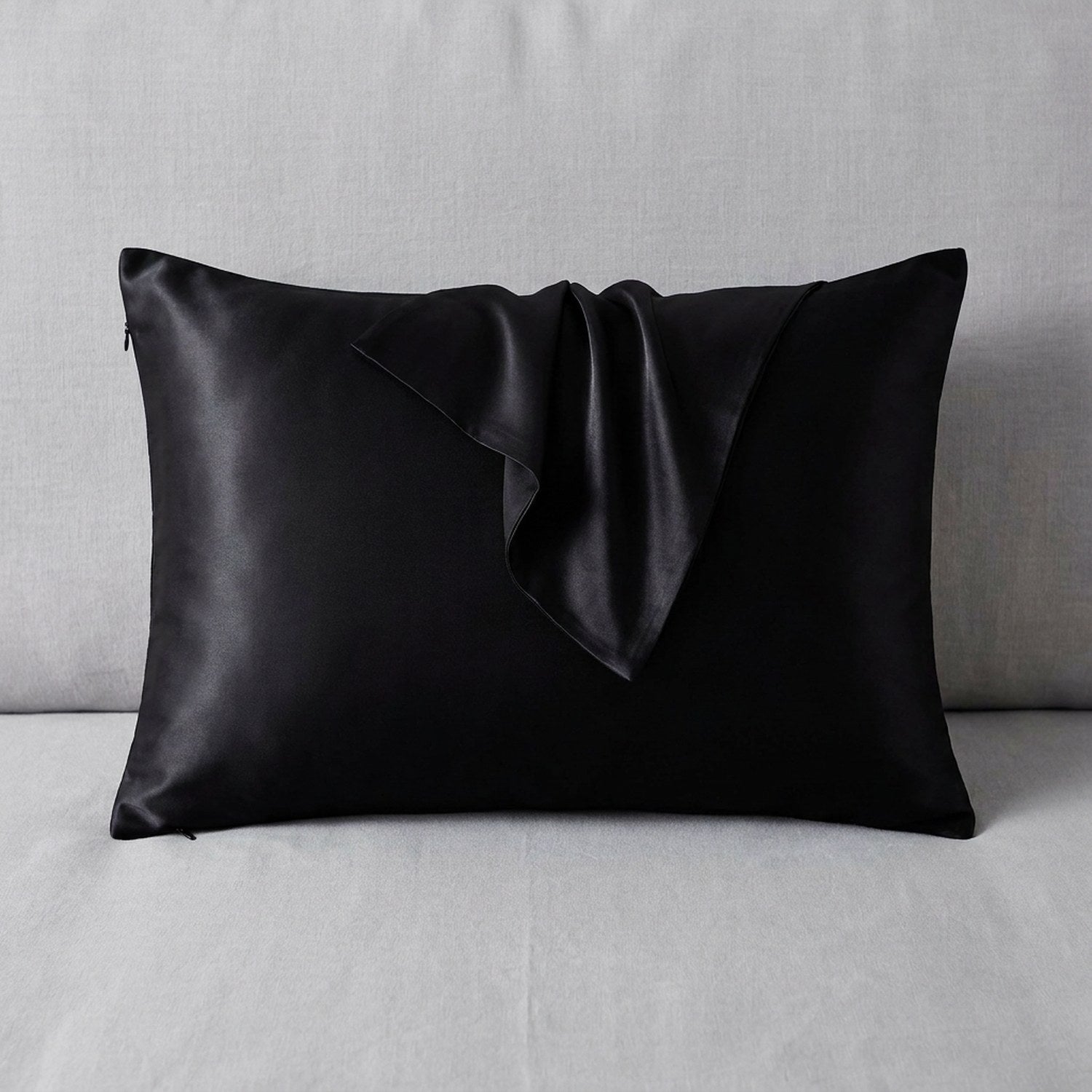 Taie d'oreiller en soie noire posée sur un tissu de lin gris clair