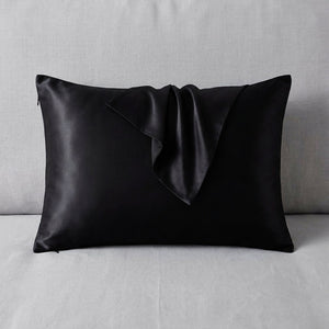 Taie d'oreiller en soie noire posée sur un tissu de lin gris clair