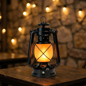 Lanterne vintage finition noire avec verre orangé façon flamme posée sur une table en bois