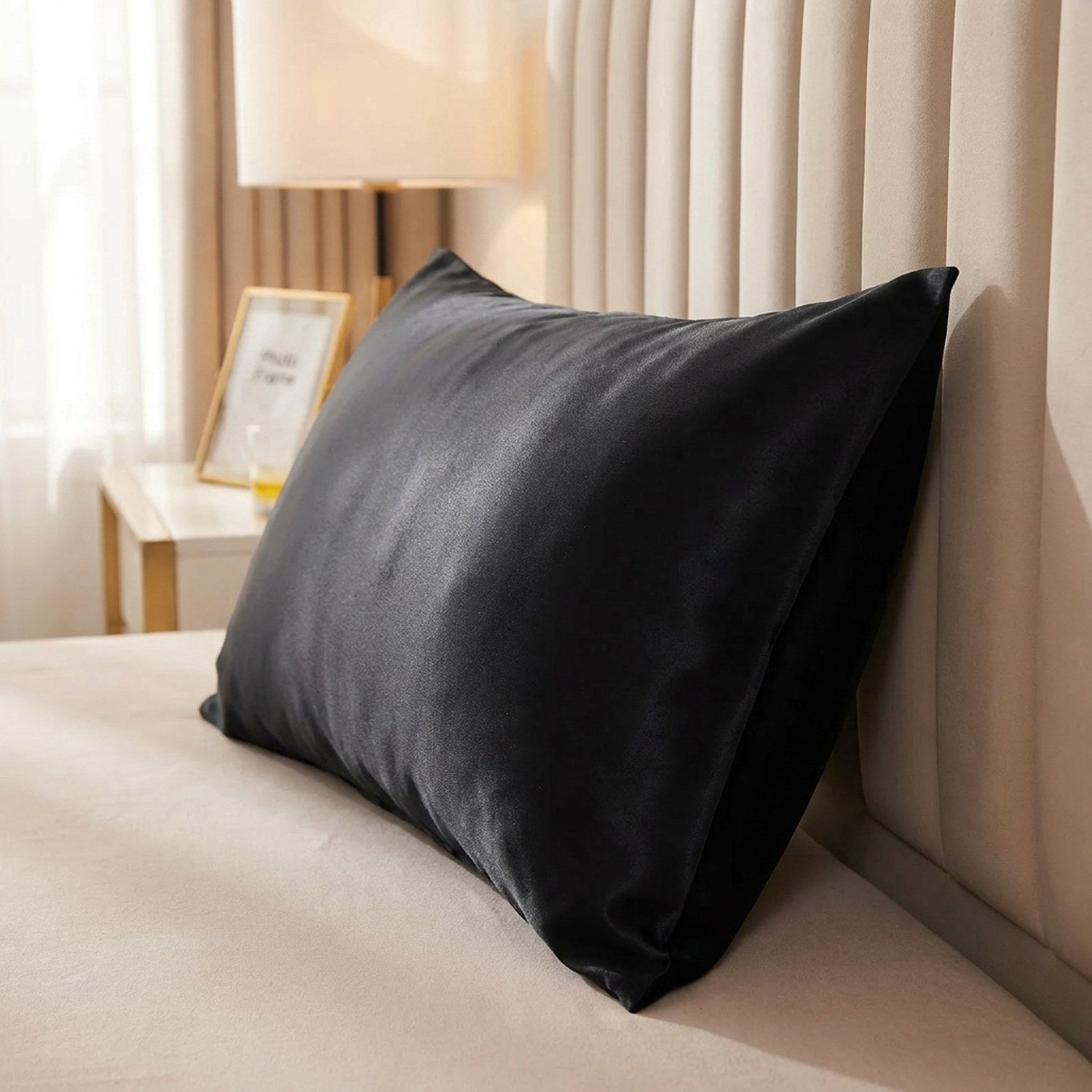 Taie d'oreiller satin noire posée sur un lit contre une tête de lit