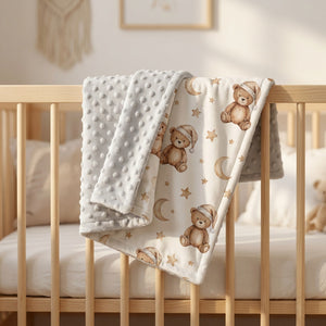 Couverture bébé minky réversible grise à motif oursons pliée sur un lit à barreaux