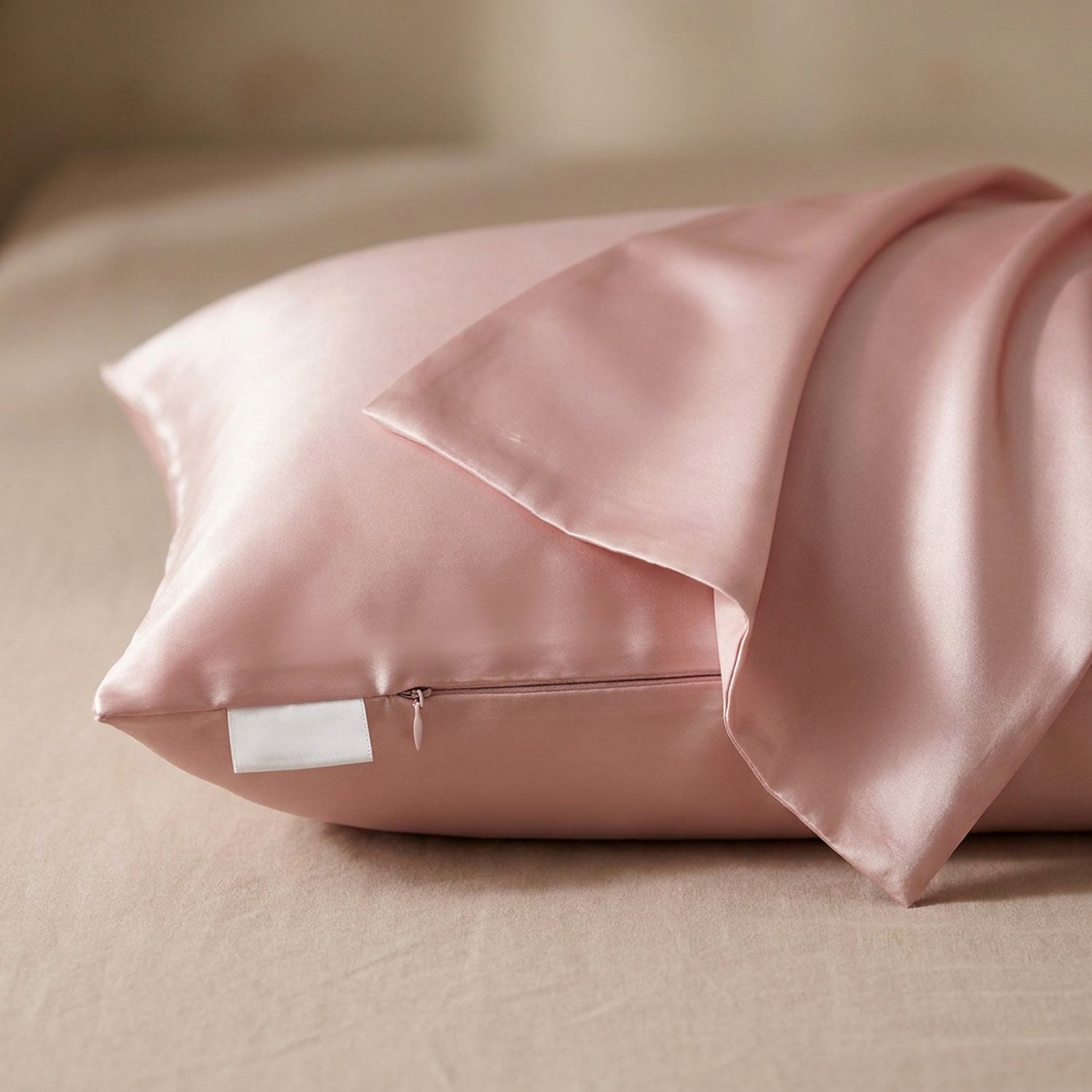 Taie d'oreiller en soie rose posée sur un tissu de lin beige