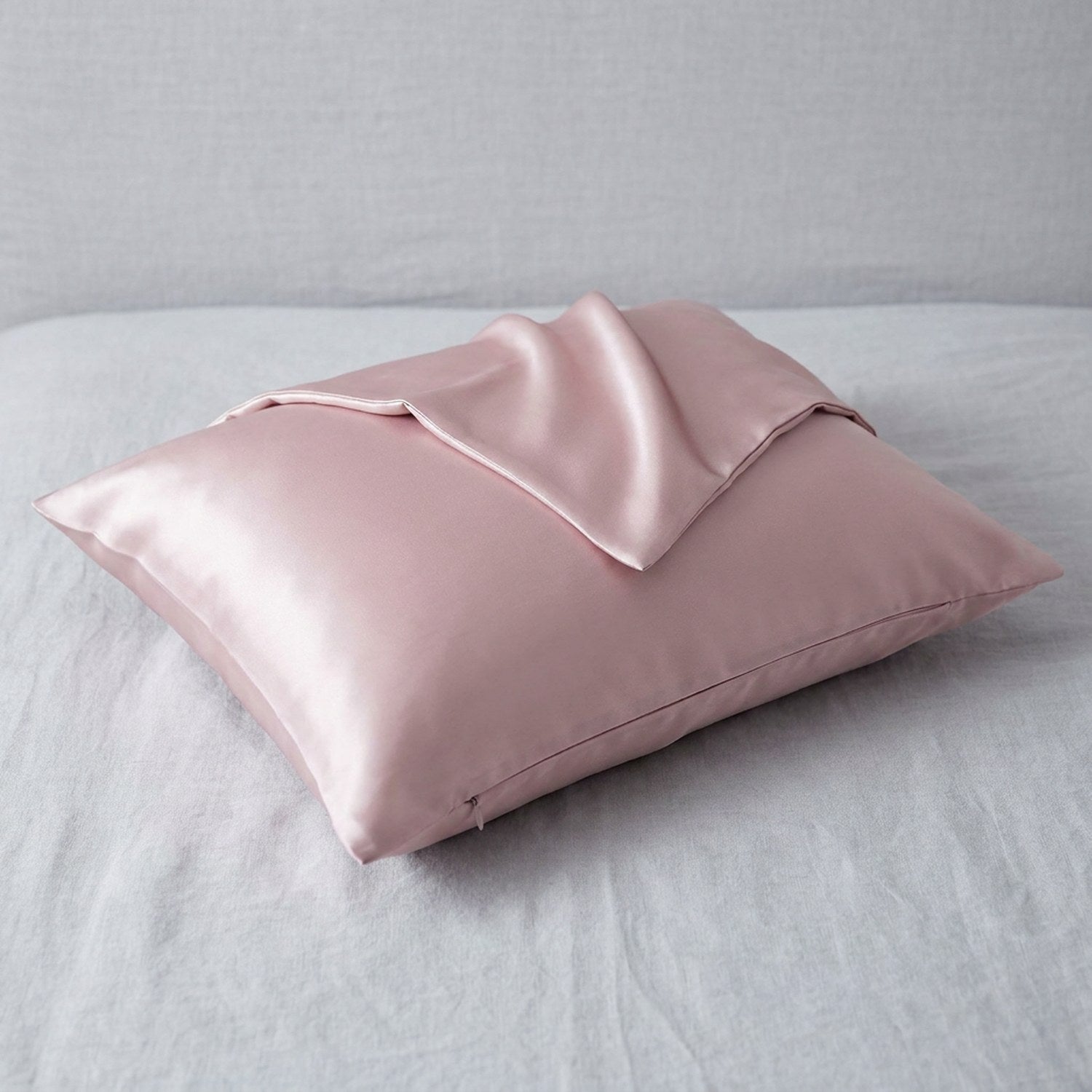 Taie d'oreiller en soie rose poudré posée sur un tissu de lin gris clair