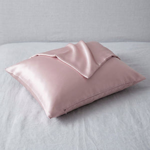 Taie d'oreiller en soie rose poudré posée sur un tissu de lin gris clair