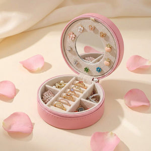 Coffret à bijoux de voyage rose ouvert entouré de pétales de rose avec boucles d'oreilles fleuries
