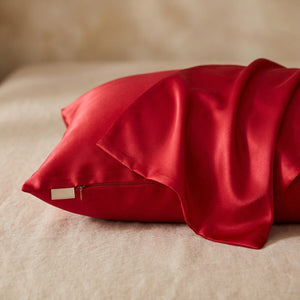 Taie d'oreiller en soie rouge posée sur un tissu de lin beige