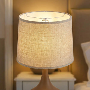 Abat-jour tambour tissu lin beige en gros plan avec texture visible et lumière chaude