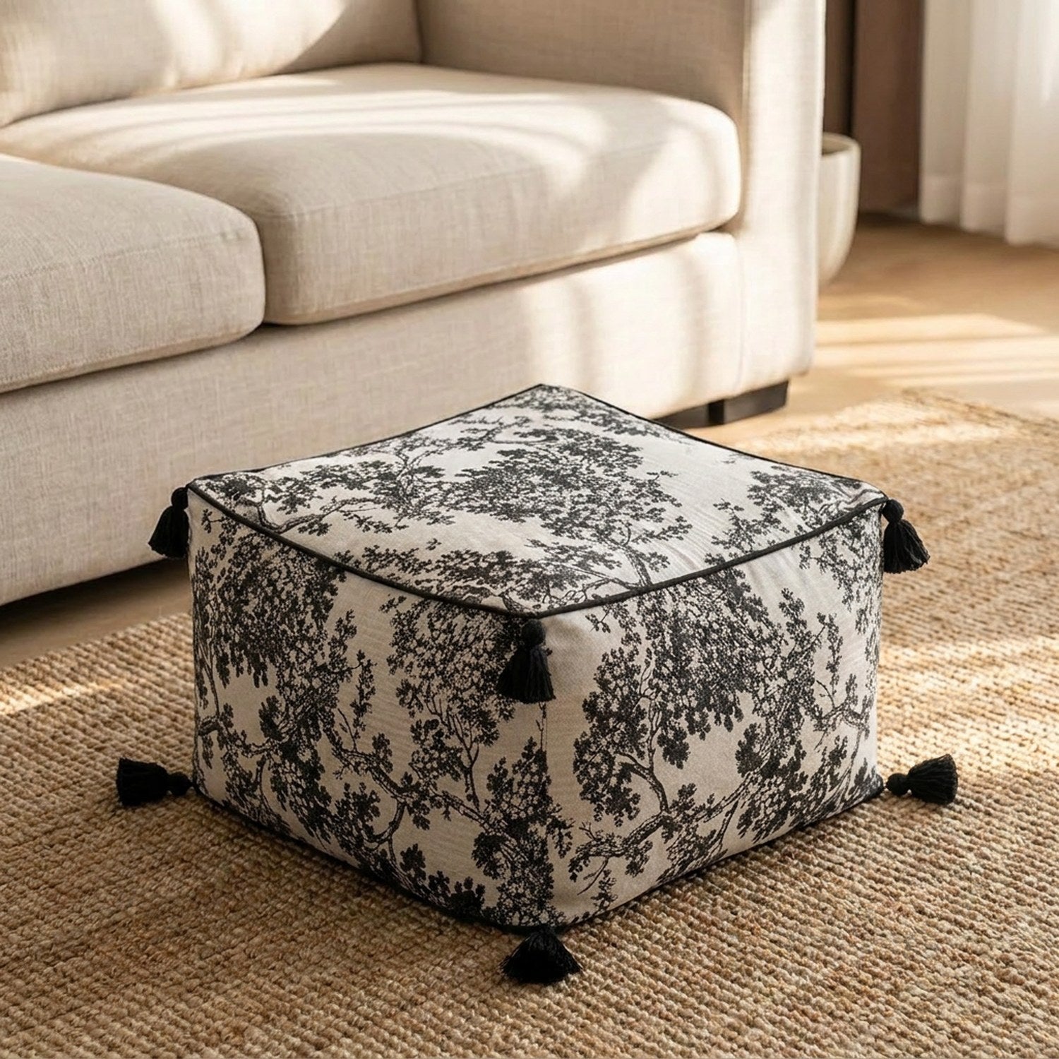 Pouf carré toile de Jouy noir et blanc posé au sol devant un canapé beige