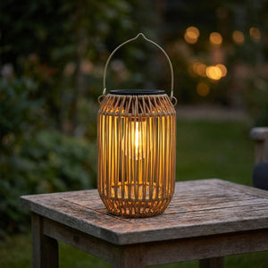 Lanterne solaire en bambou tressé forme cylindrique posée sur une table en bois