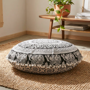 Housse de coussin ronde motif éléphant noir et blanc posée sur un tapis bohème