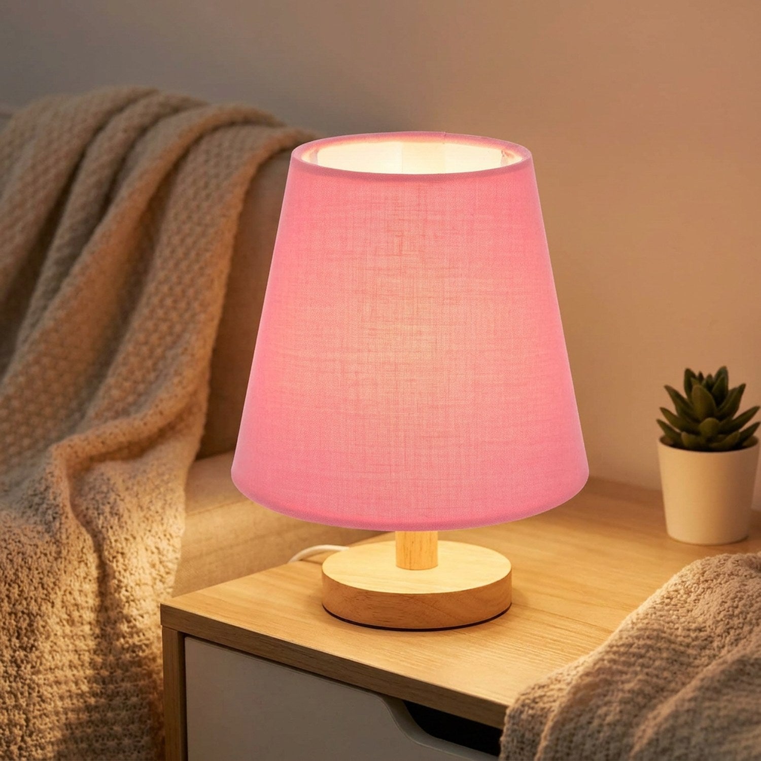 Abat-jour en tissu conique rose sur une lampe de chevet en bois allumee