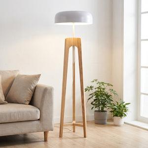 lampadaire trépied en bois clair au dôme blanc allumé dans un salon scandinave