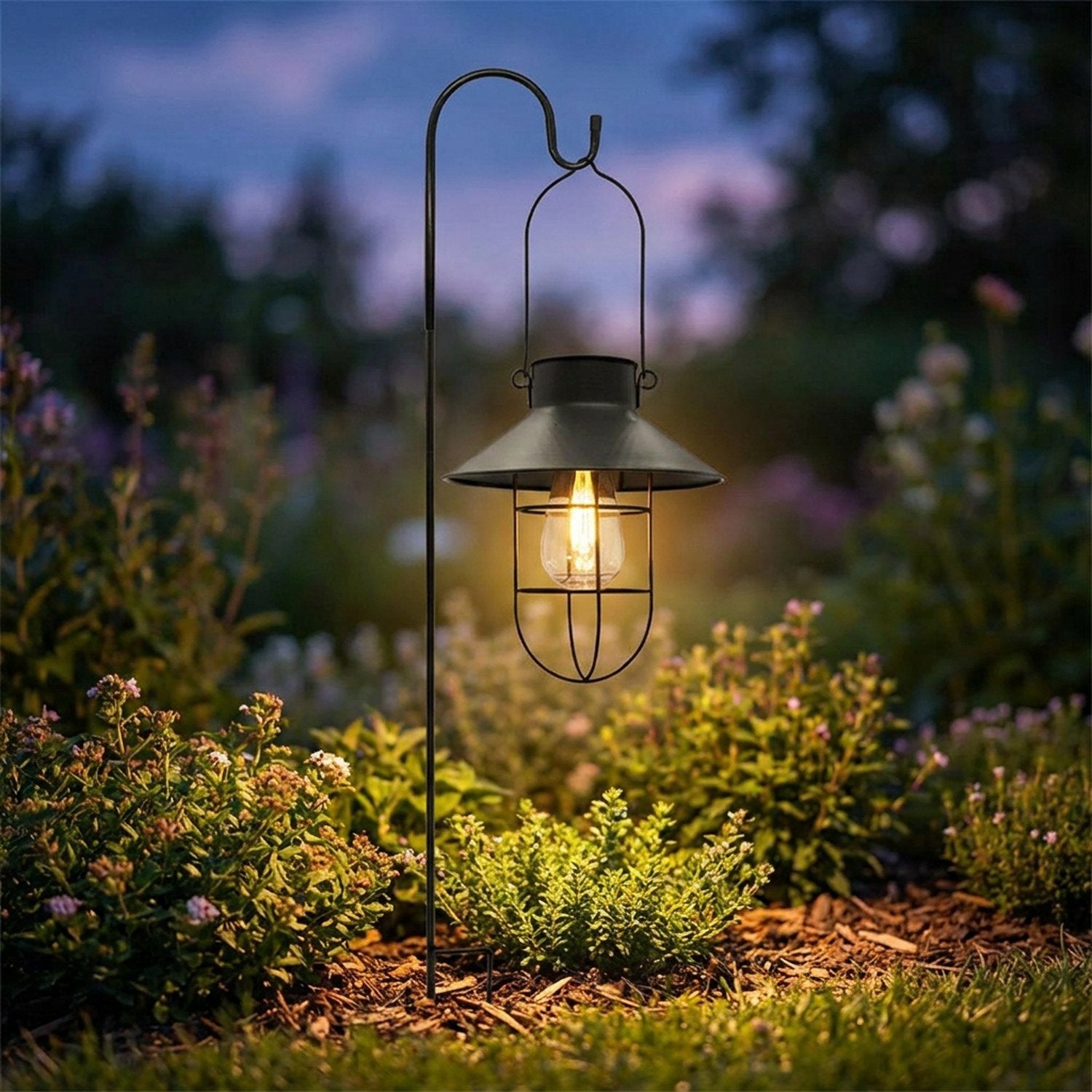 Lanterne solaire noire allumée sur un piquet de jardin planté dans un massif