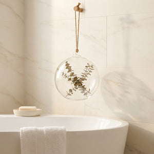Vase boule en verre suspendu dans une salle de bain avec baignoire et carrelage marbre