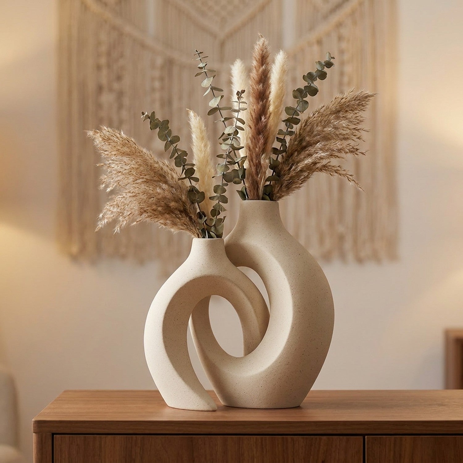 Duo de vases en céramique beige enlacés avec pampas et eucalyptus sur un buffet