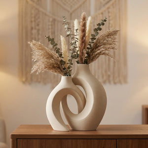 Duo de vases en céramique beige enlacés avec pampas et eucalyptus sur un buffet