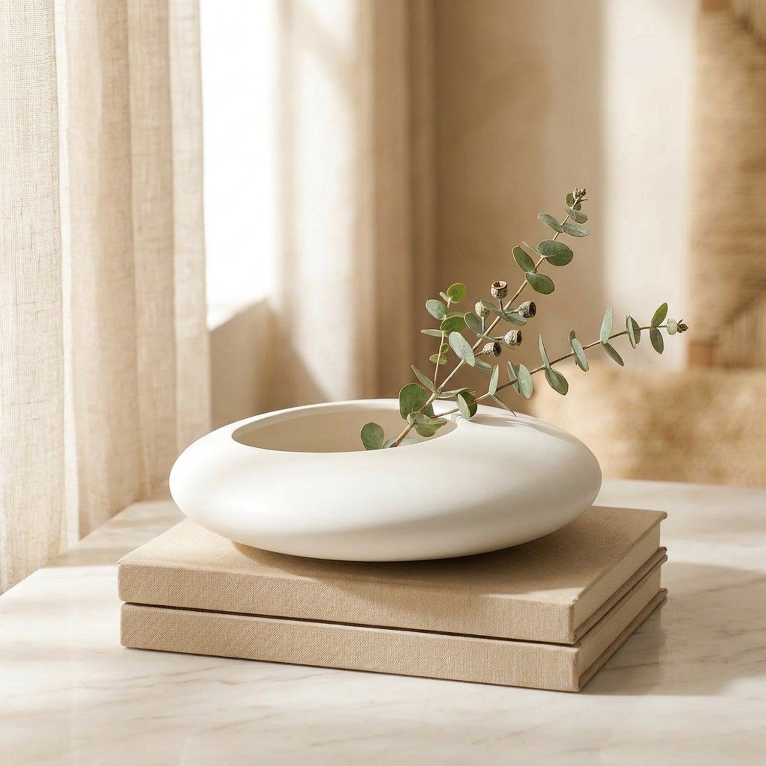 Vase galet blanc posé sur des livres près d'une fenêtre avec brin d'eucalyptus